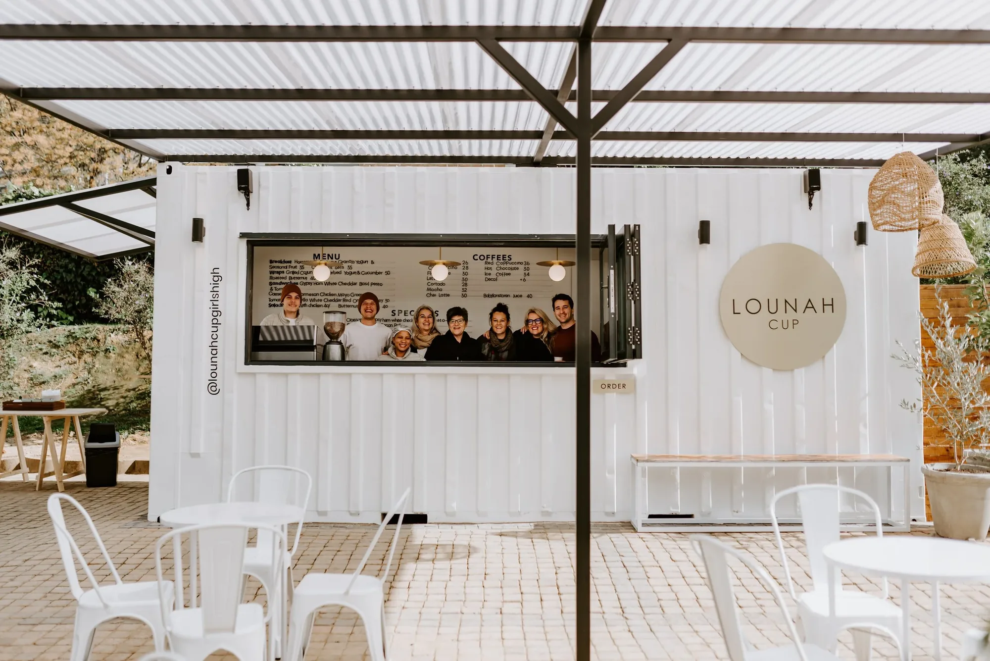 The white Lounah Cup container café with its serving hatch open, staff at the counter and tables in front.