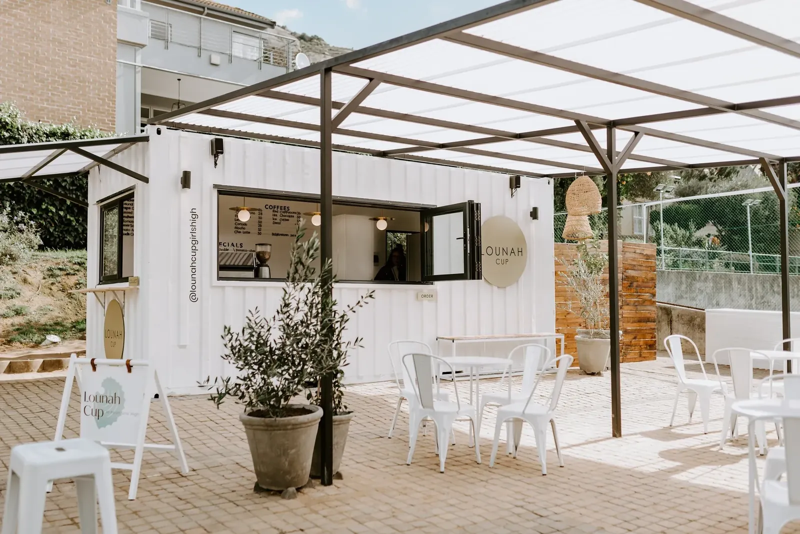 Olive planters and white chairs on the paving beside the container.