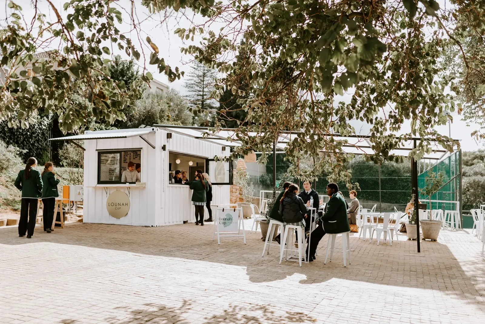 The Lounah Cup container under a pergola, with pupils at the hatch and seated at tables.