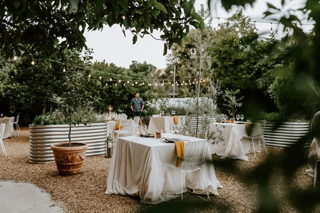 A long linen-covered dinner table set in the garden, strings of lights above.